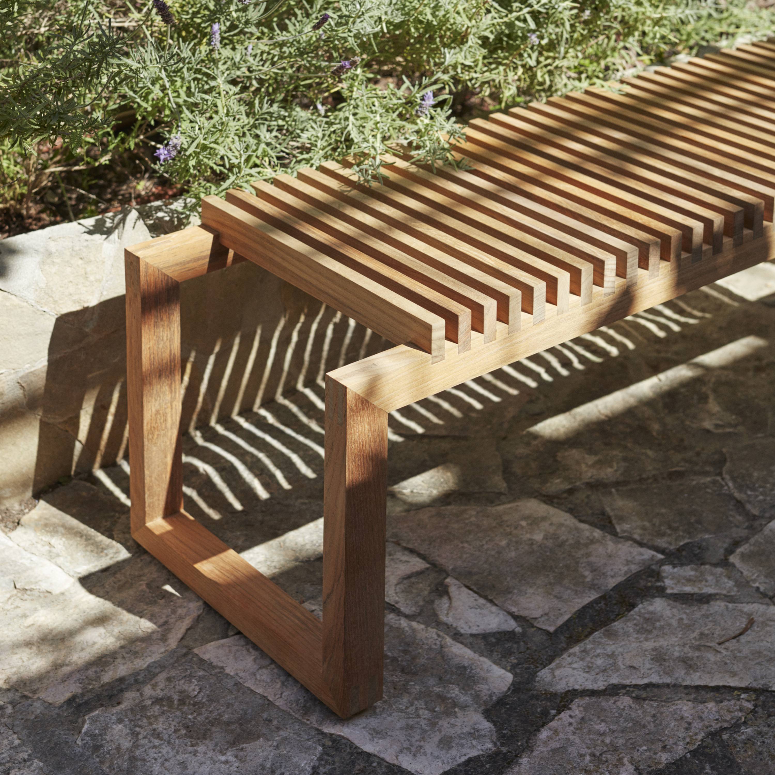 Outdoor Cutter Bench by Skagerak with wooden slats and rectangular frame on stone patio.