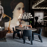 Dark quilted dining chairs around an oval table, with a chandelier and large portrait backdrop
