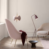 A pink pendant with two fan-shaped shades and a brass ring hangs above a pink armchair in a pale room