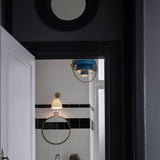 A blue tiered pendant with a brass arm hangs in a tiled bathroom beside a cream wall light