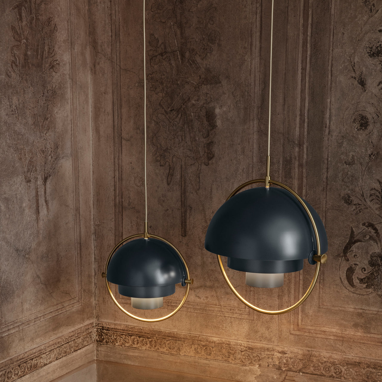 Two dark blue domed pendants with brass rings hang in a room with weathered, ornate painted walls