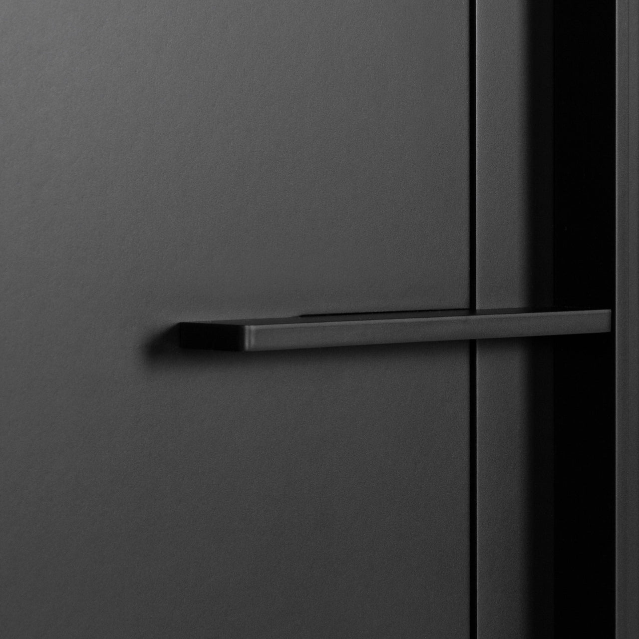 Close-up of a slim black horizontal bar handle on a matte black cabinet door