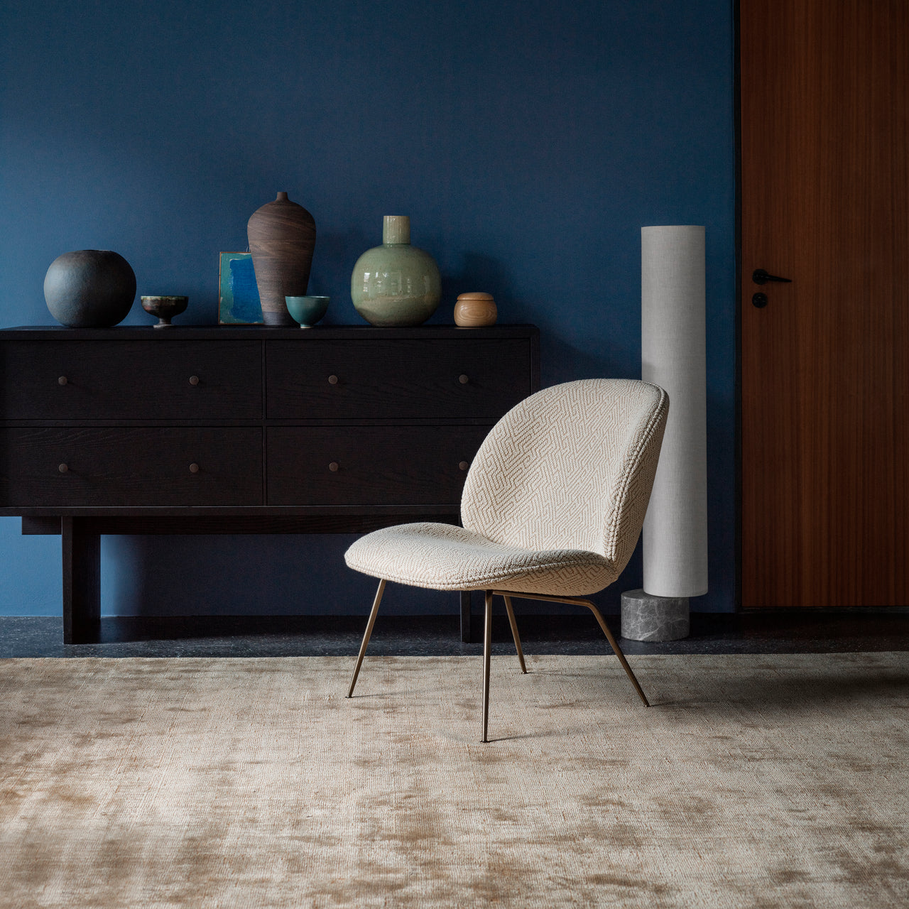 A dark wood sideboard with six drawers against a deep blue wall, with a cream patterned chair in front