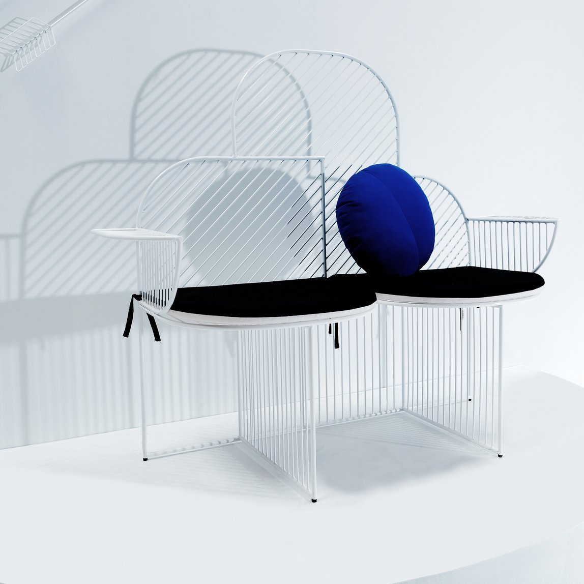 Electric blue wireframe Cloud Bench with black seat cushions and a round electric blue back cushion on right seat.